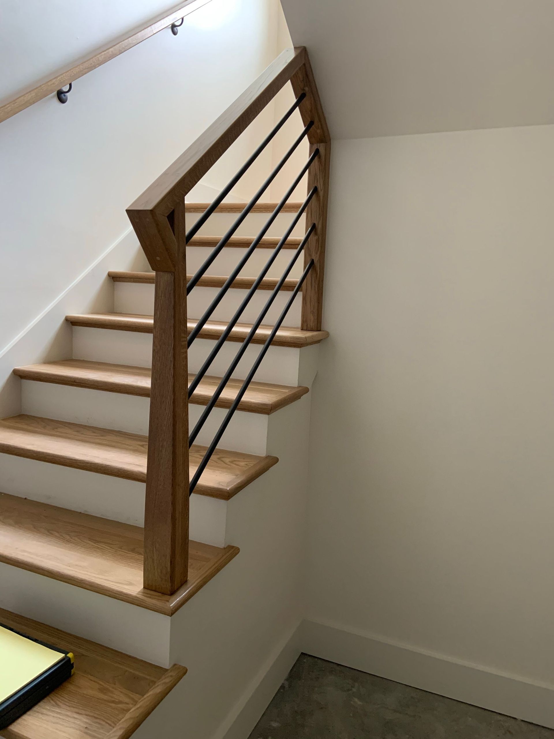 Modern staircase with white oak treads, white risers, and a square oak handrail with horizontal black metal rod balusters