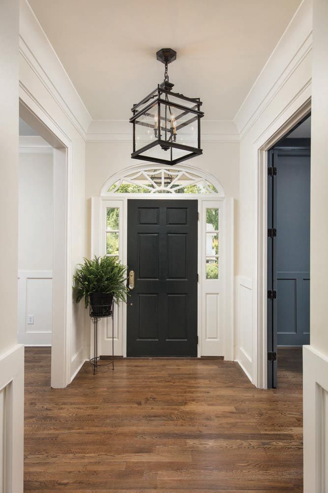 Hallway with dark wood floor, black front door, white trim, and hanging lantern.
