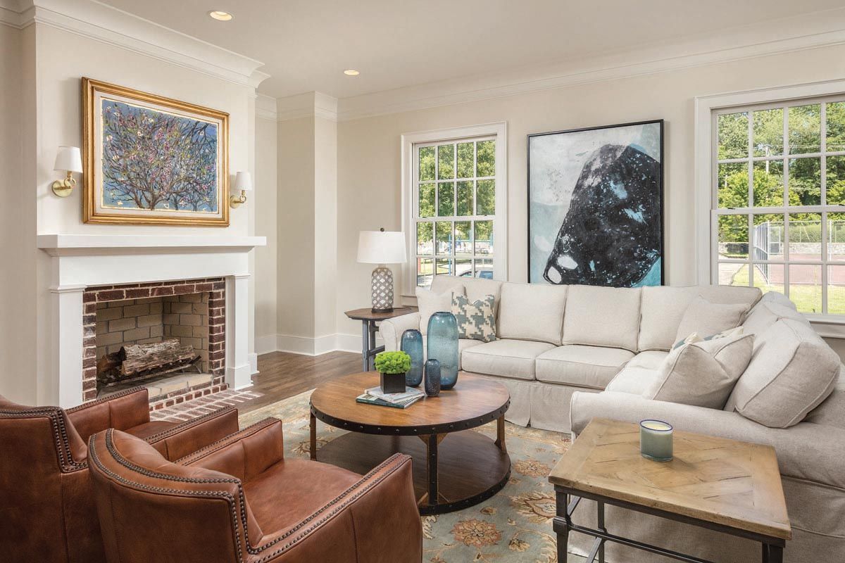 Living room with fireplace, white walls, leather armchairs, sectional sofa, and colorful artwork.
