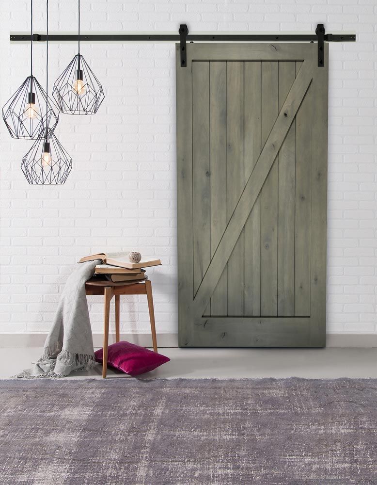 Gray barn door with black hardware, next to a stool with blanket and pillow.
