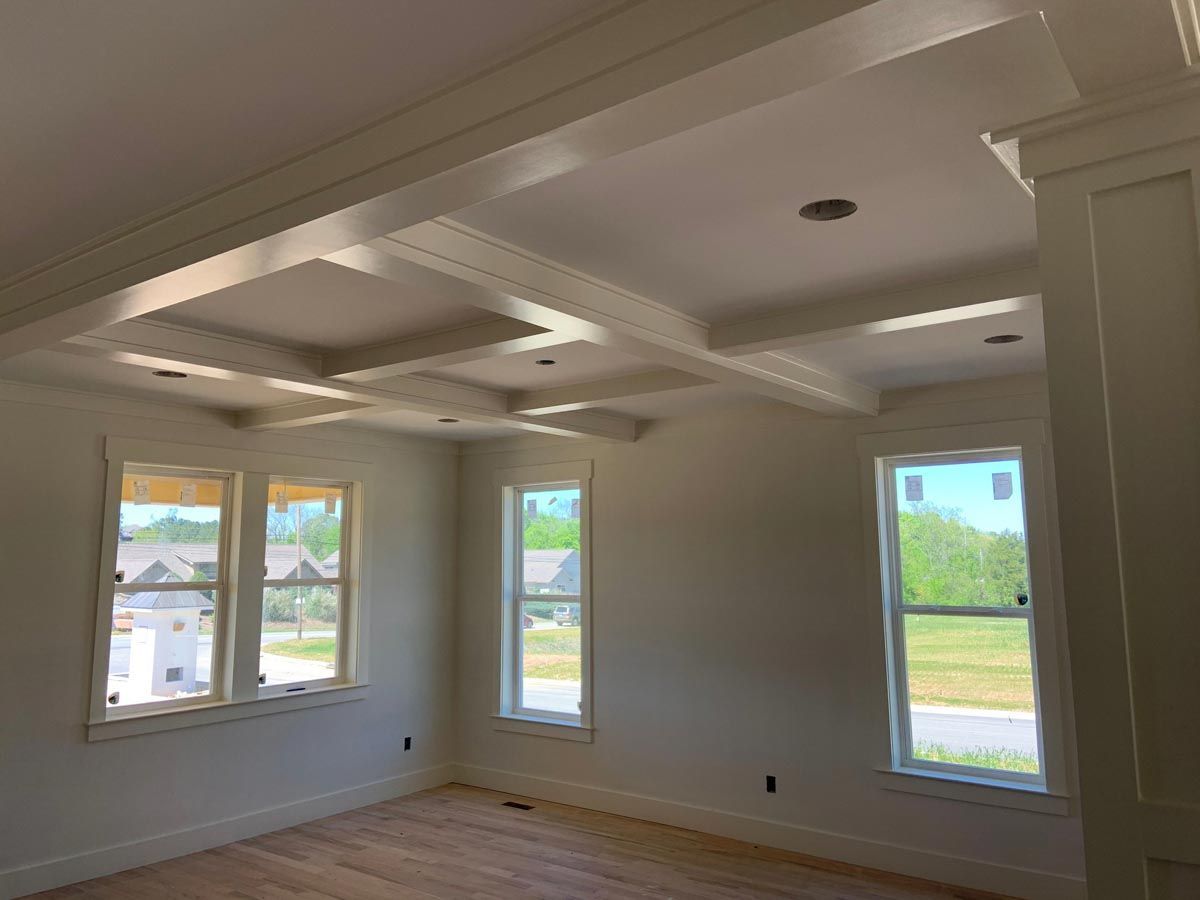Empty room with coffered ceiling, three windows, and white trim.