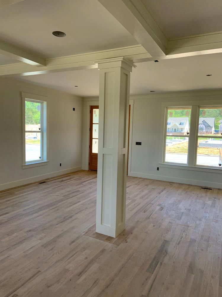 Bright interior of a new home with hardwood floors, white trim, windows, and a decorative column.