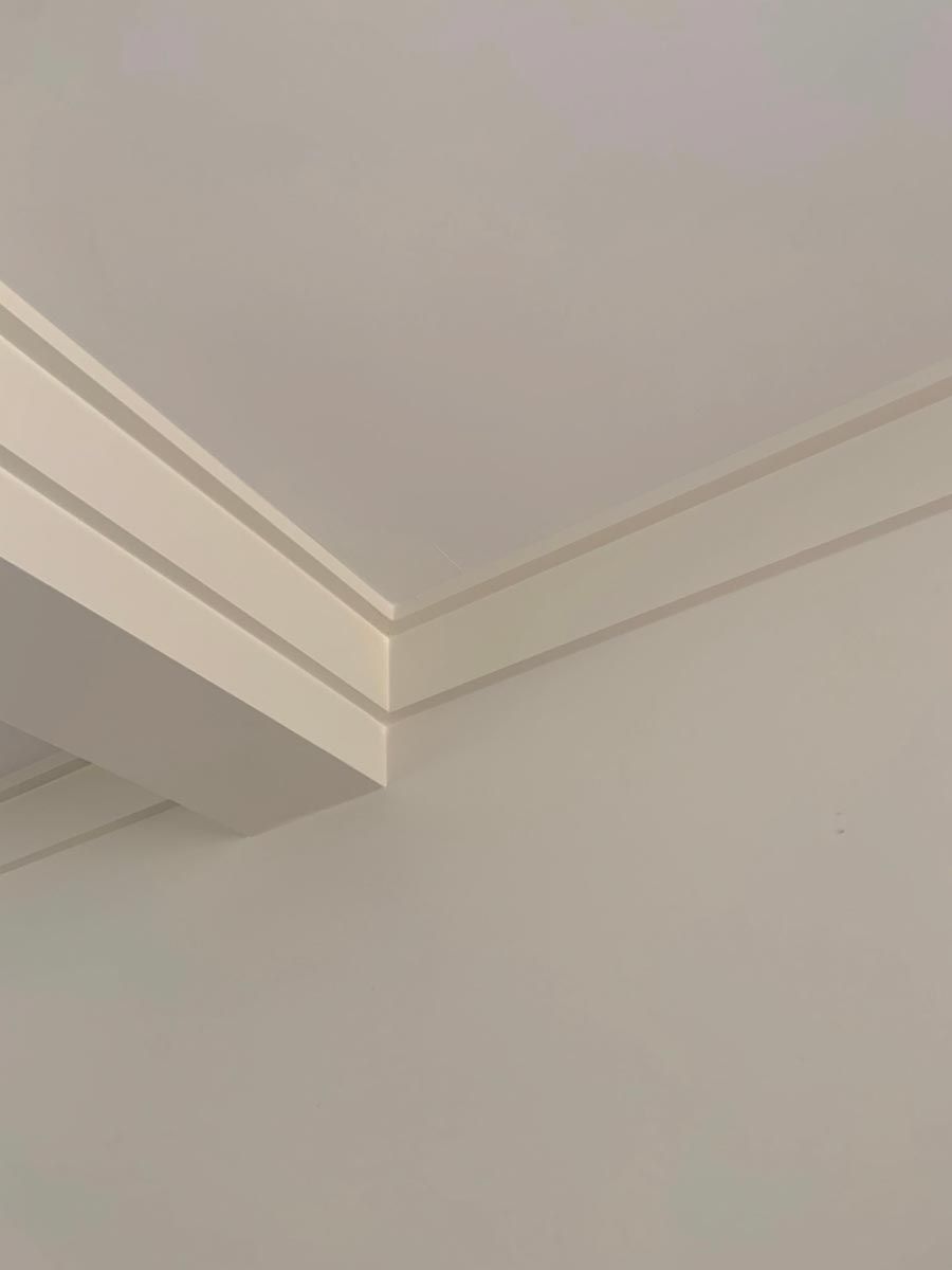 Corner of a white ceiling with layered crown molding, casting a shadow.