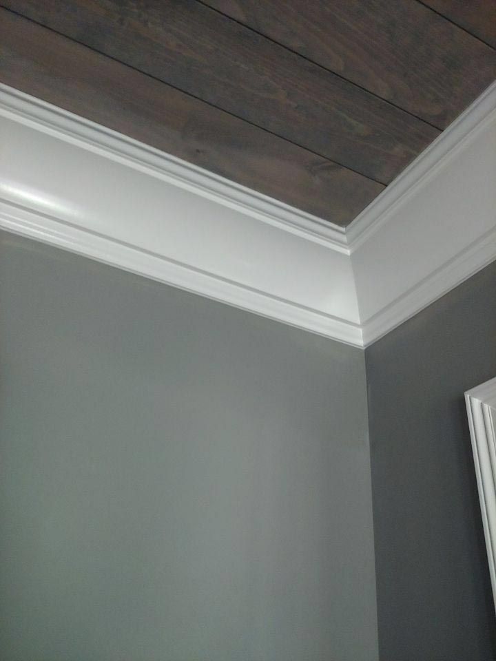 White crown molding meets grey walls and wood-grain ceiling at a corner.