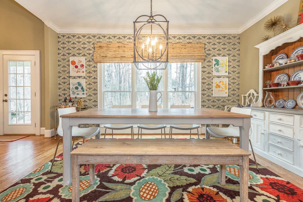 Dining room with wooden table, floral rug, and botanical wallpaper.