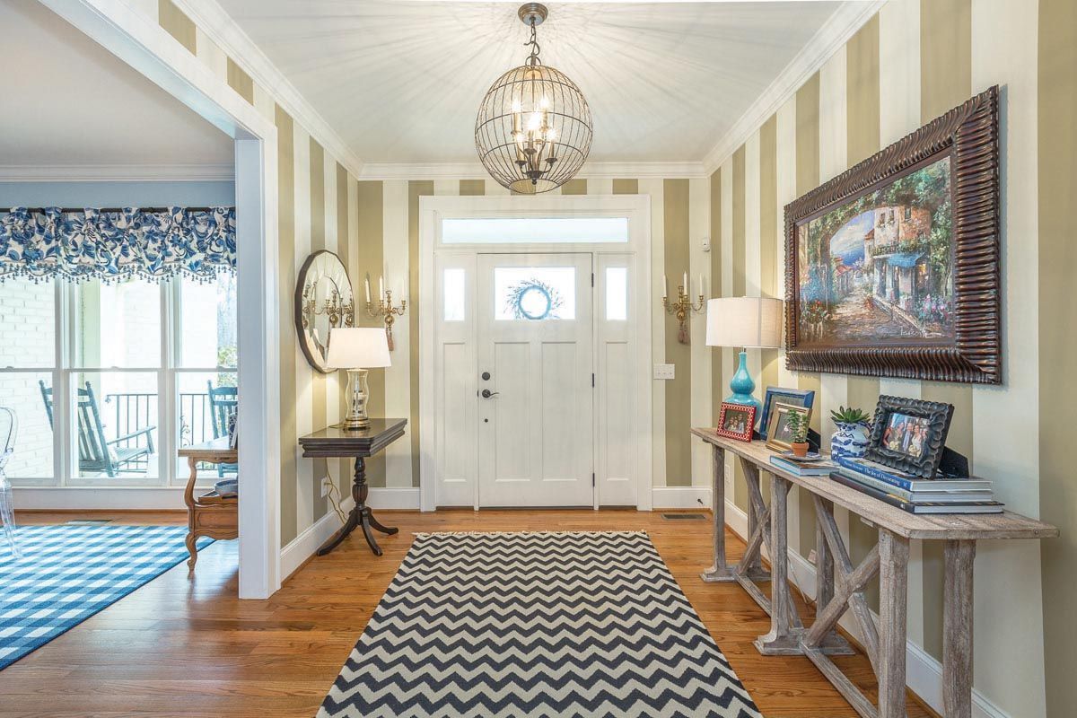 Inside entryway to a home with beige and white striped walls, a zig zag rug, and a chandelier.