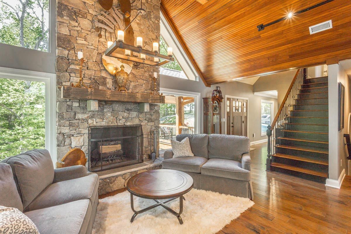Cozy living room with stone fireplace, wood ceiling, gray sofas, and a round coffee table on a fluffy rug.
