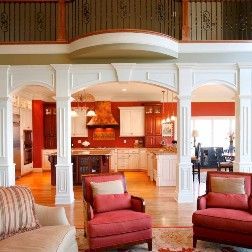 Living room with archways, red chairs, and a view into a red and white kitchen.