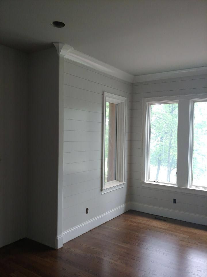 Empty room with wood floors, windows, and shiplap wall. White trim and crown molding.