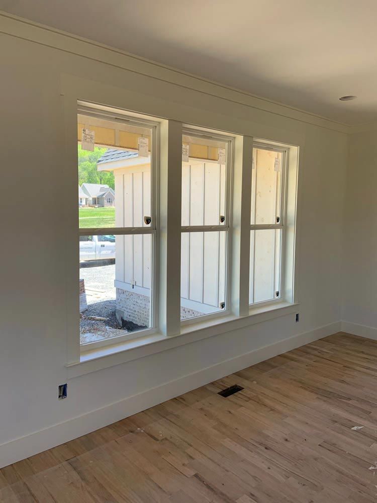Three white framed windows in a room with hardwood floors and white walls.