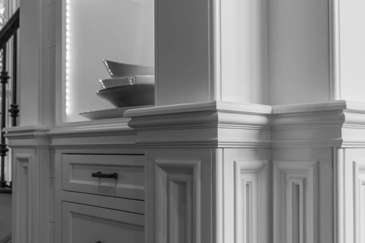 White built-in cabinet with decorative molding, drawers, and stacked bowls. Sunlight casts shadows.
