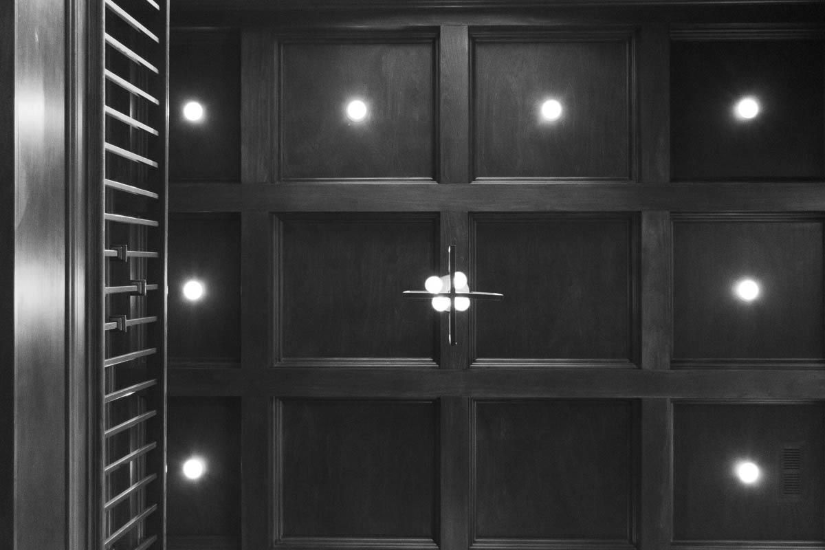 Black and white view of a dark wooden coffered ceiling with inset lights.