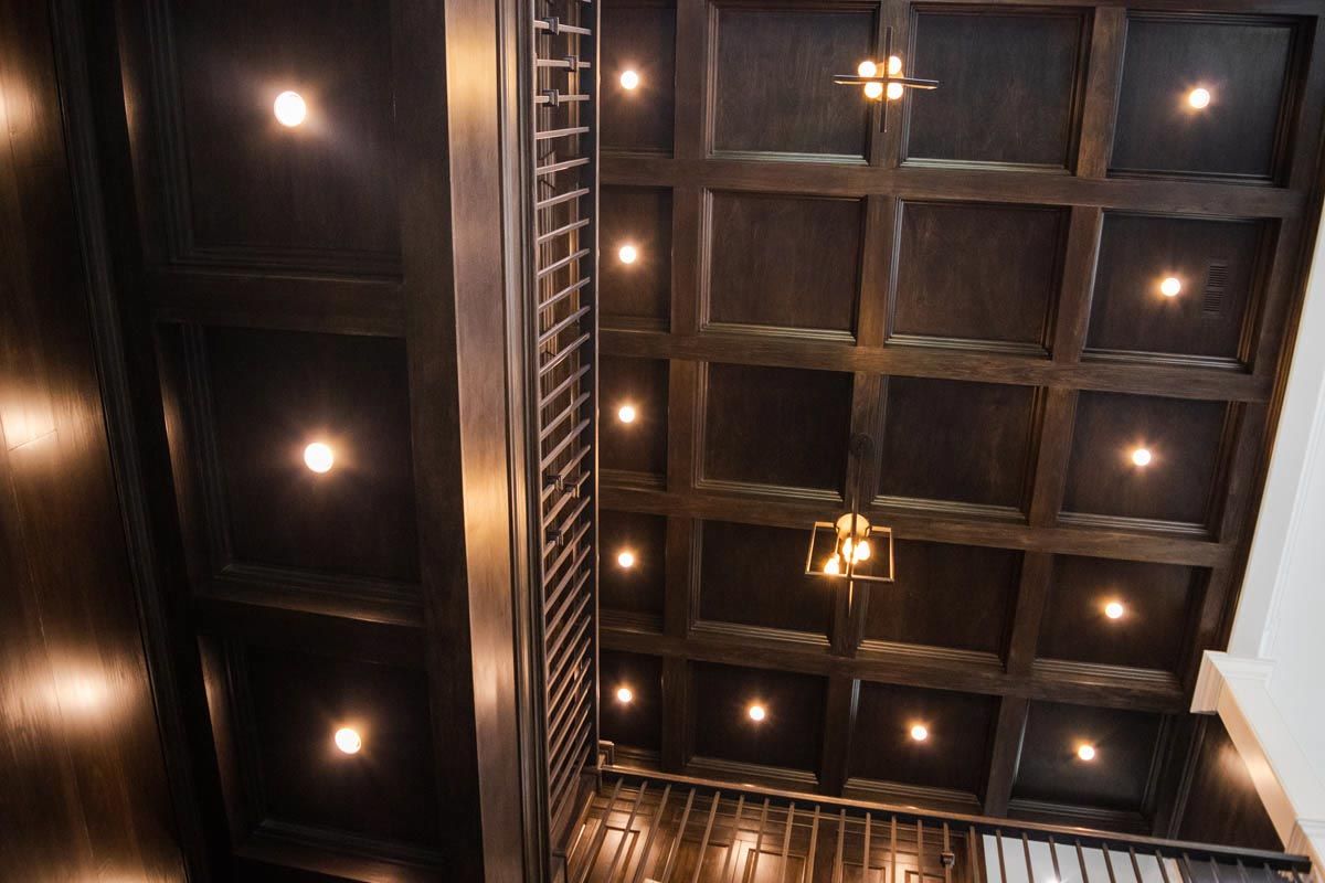 Dark wood paneled ceiling with recessed lights and a staircase visible.