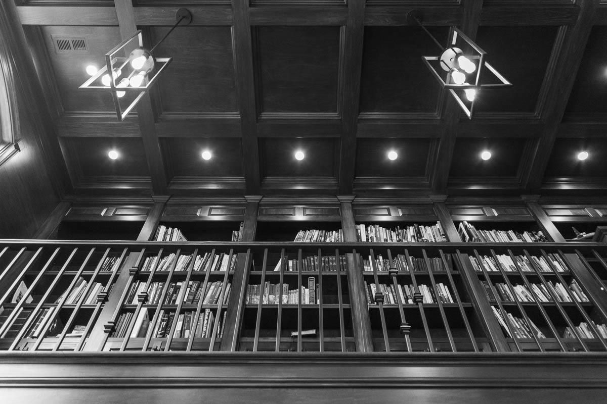 Bookshelves filled with books, railing, coffered ceiling, pendant lights, library interior.