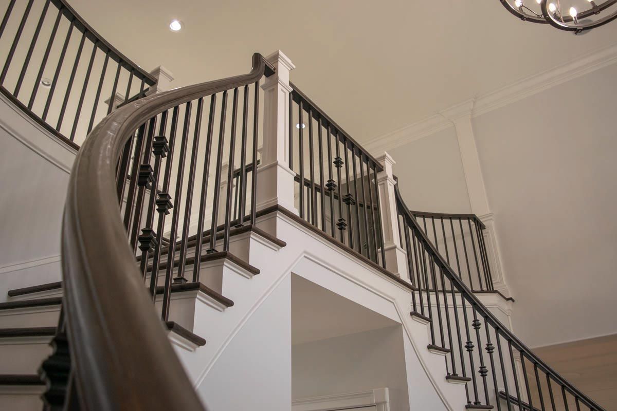 Curving staircase with dark wooden handrail, white risers, and black iron balusters.