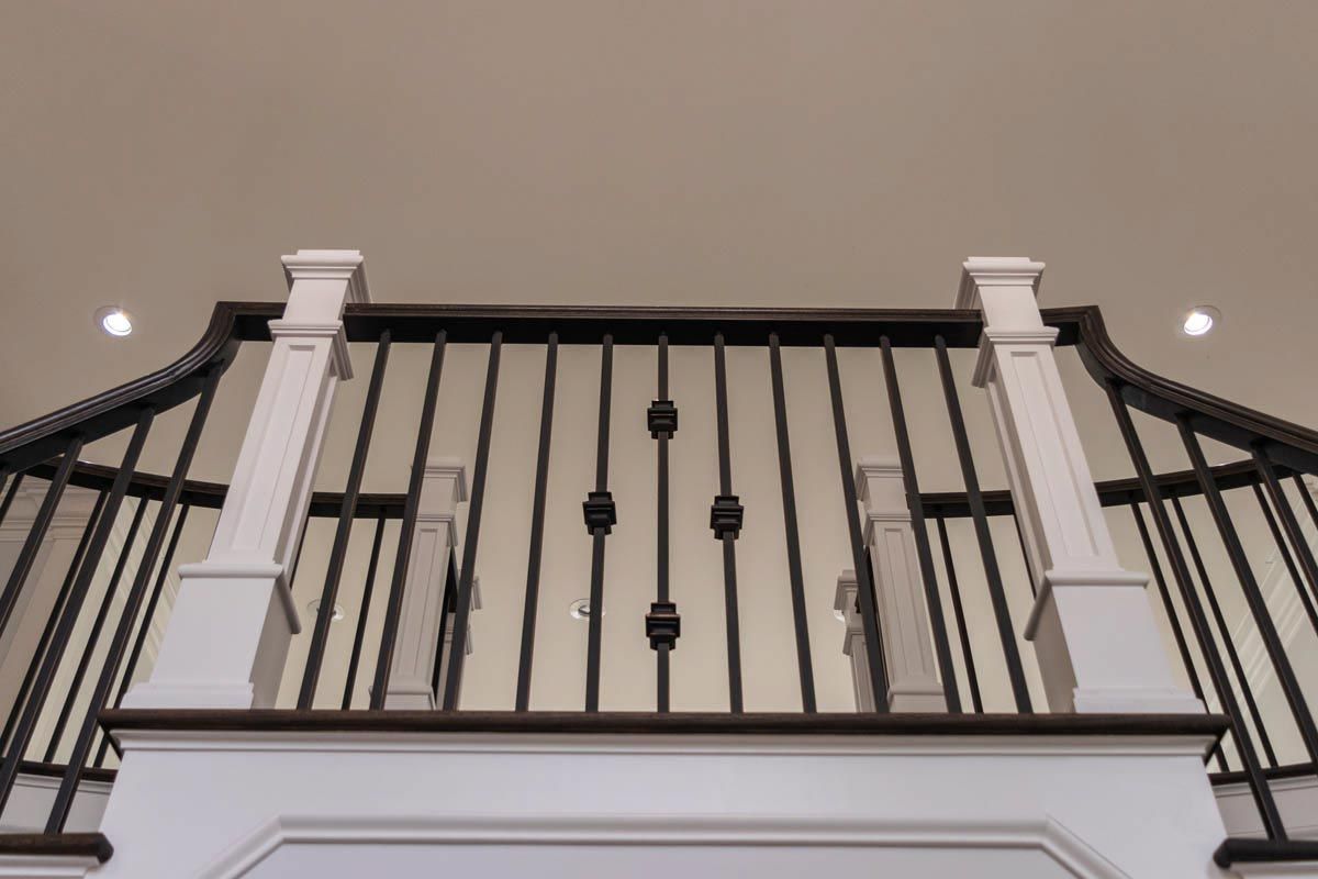 Looking up at a staircase railing with white posts, dark spindles, and a light-colored ceiling.