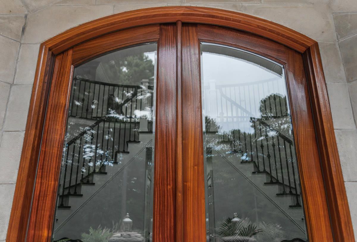 Large wood exterior doors with large glass panels looking into a home with a double staircasre/