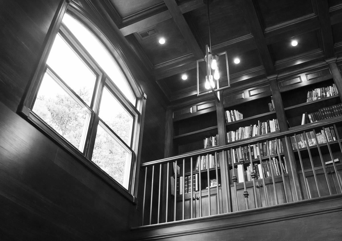 Library interior with arched window, bookshelves, and railing.