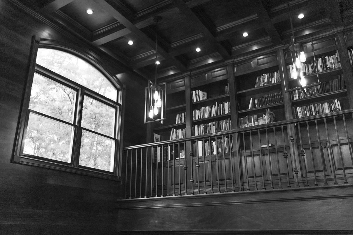 A dark wood library with built-in bookshelves, arched window, and overhead lighting.