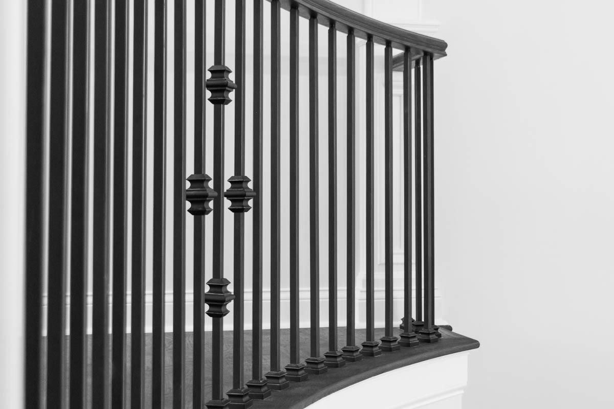 Black wrought iron banister with decorative elements, curved, against a white wall.