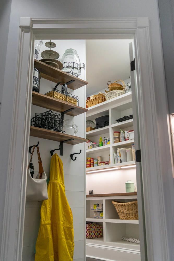 Open pantry with wooden shelves, baskets, and canned goods. Yellow raincoat and bag hang on the left.