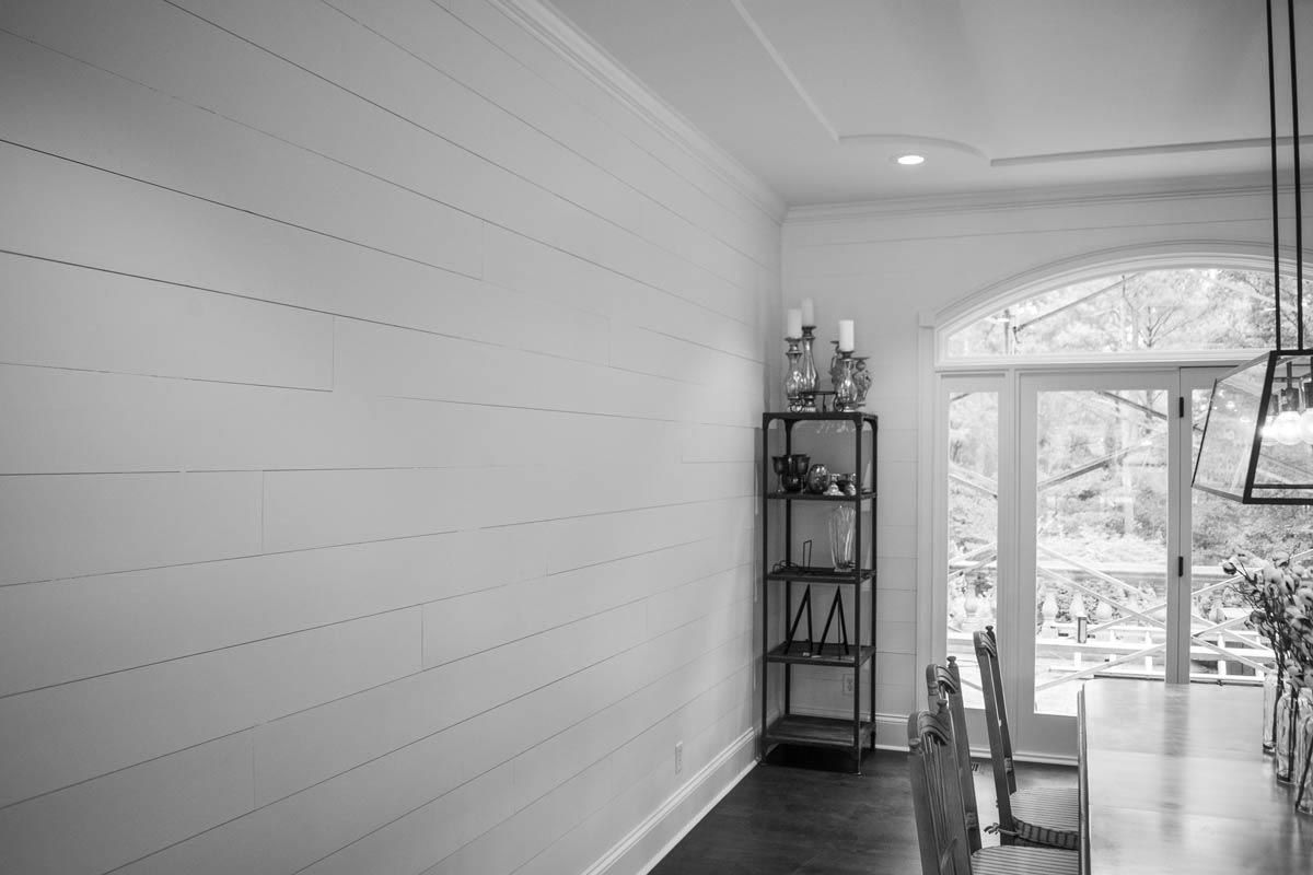 White-paneled wall and doorway in dining room with a long table and wrought iron shelving.