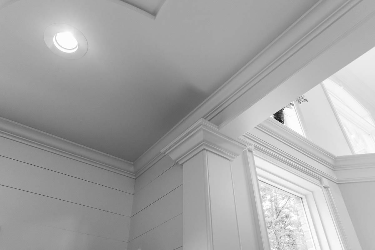 White ceiling with recessed lighting and detailed crown molding surrounding a window.