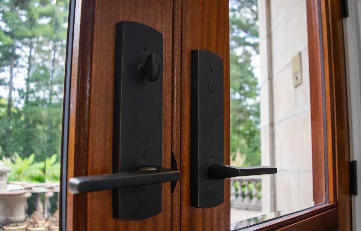 Close up of black exterior door hardware on dark wood double doors.