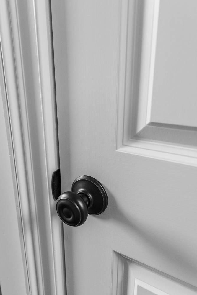 Black and white close-up of a white door with a dark doorknob. The door is slightly ajar.