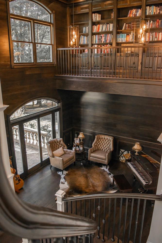 Library with two-story bookshelves, seating area, piano, and large window overlooking a balcony.