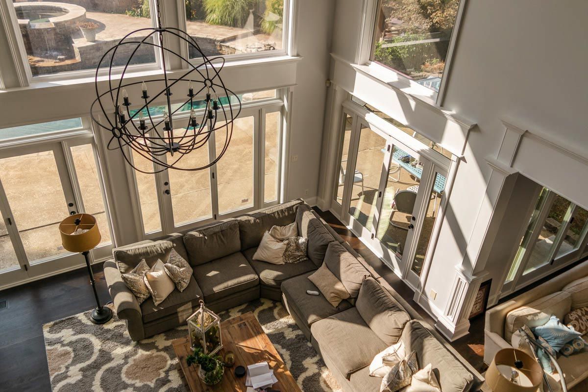 High-angle view of a living room with an L-shaped sofa, large windows, and a chandelier.