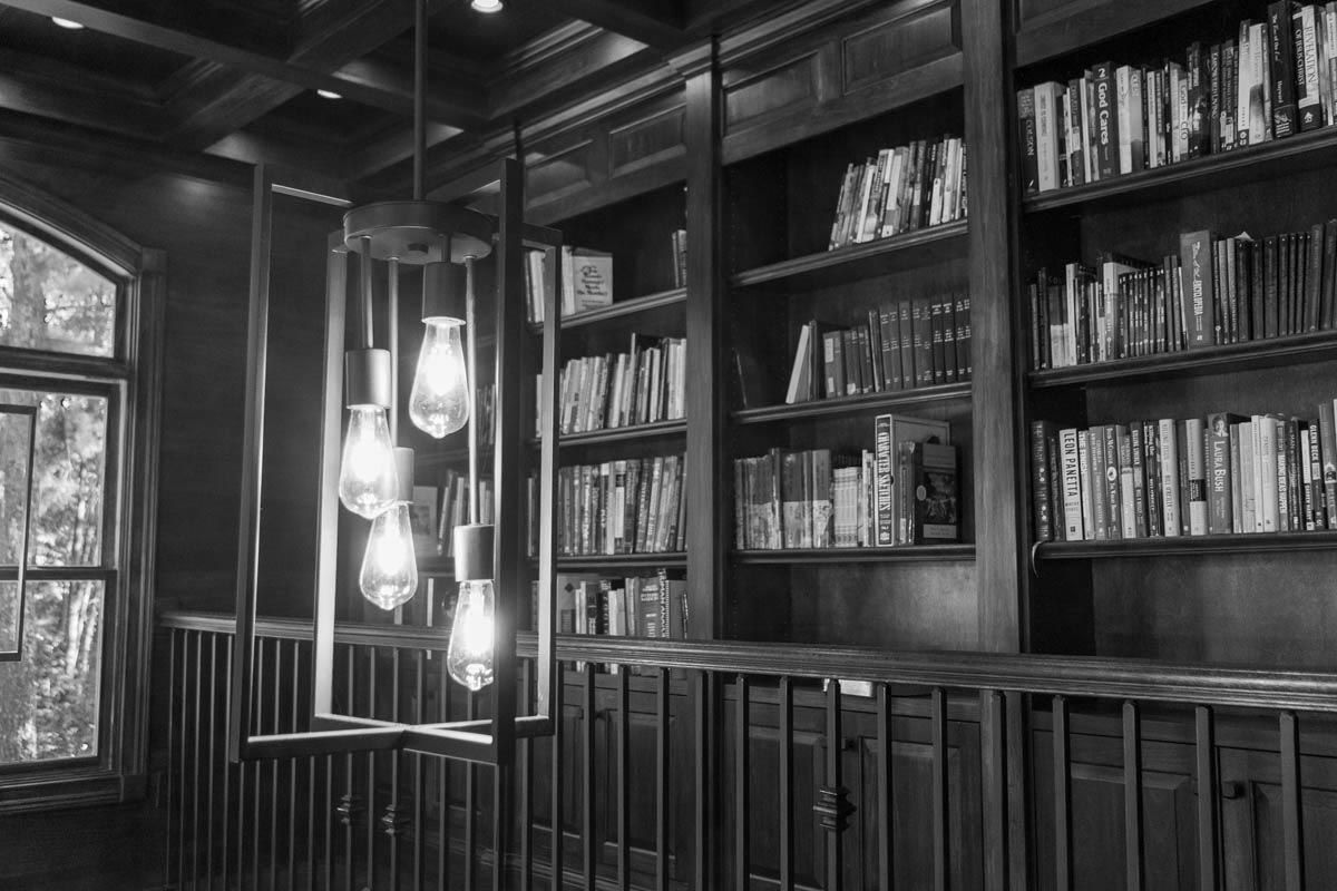 Bookshelves filled with books, pendant lights, and a window in a dimly lit library.