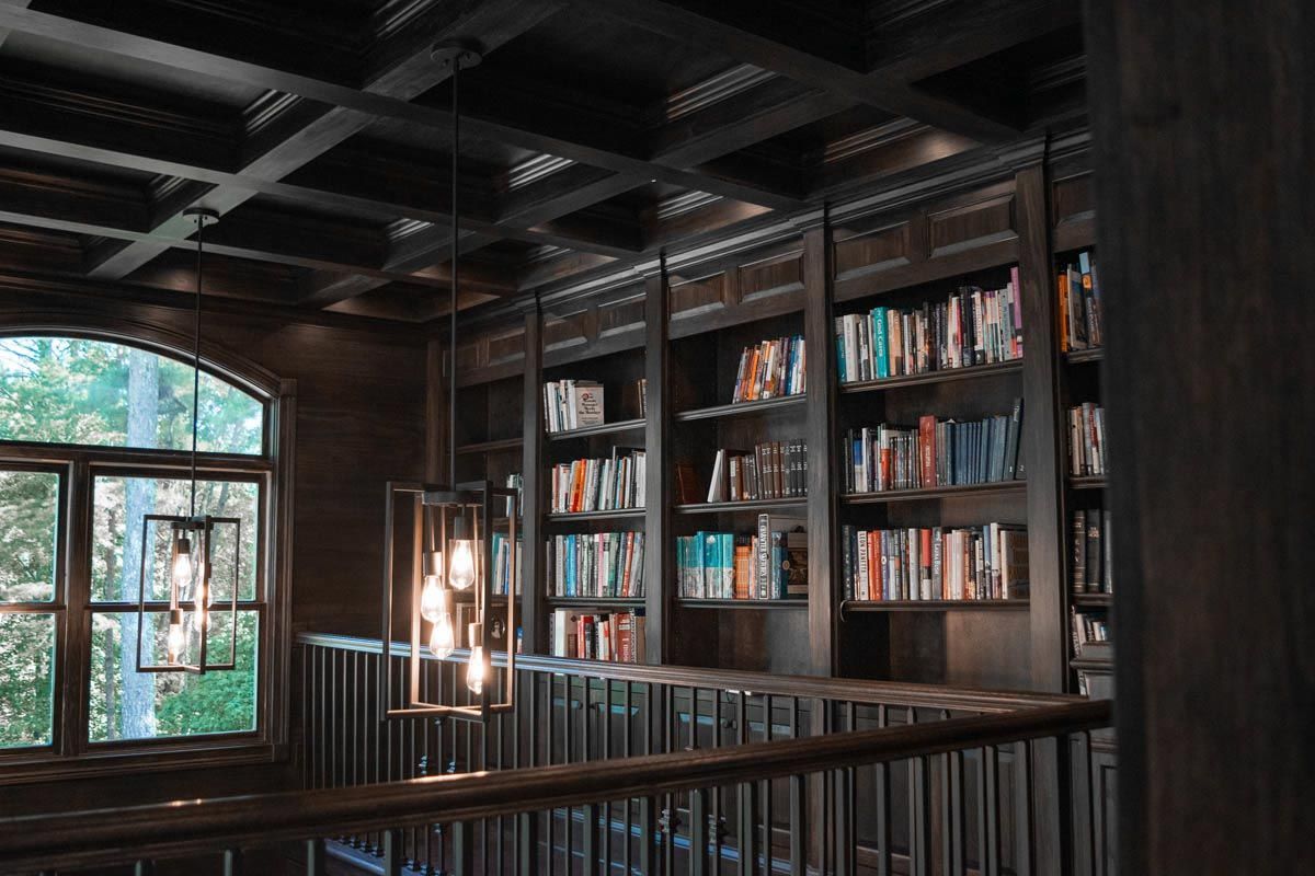 Dark wood library with bookshelves, arched window, and hanging light fixture.