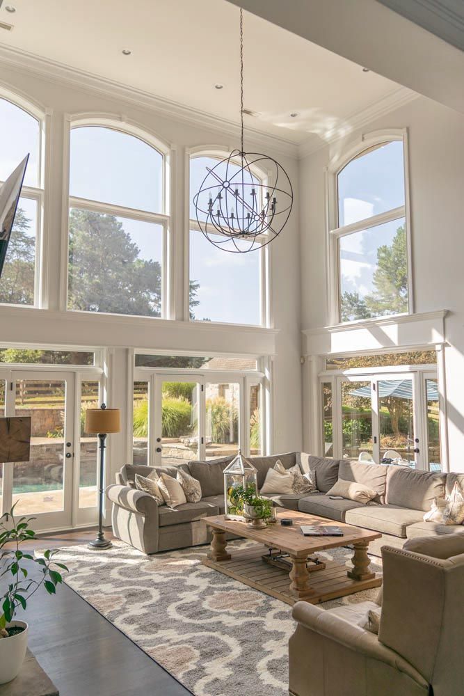 High-ceilinged living room with large windows, a gray sectional sofa, and a wooden coffee table.
