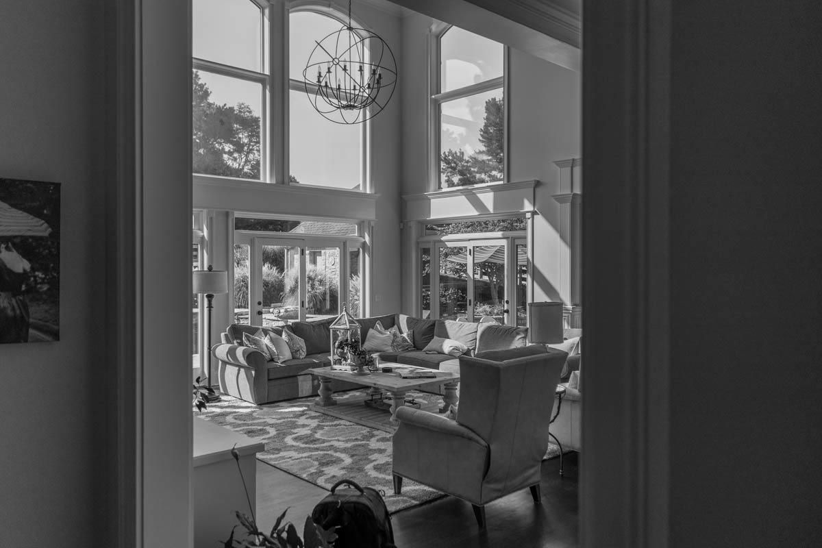 Living room with large windows, bright light, and a chandelier; a glimpse from a doorway.