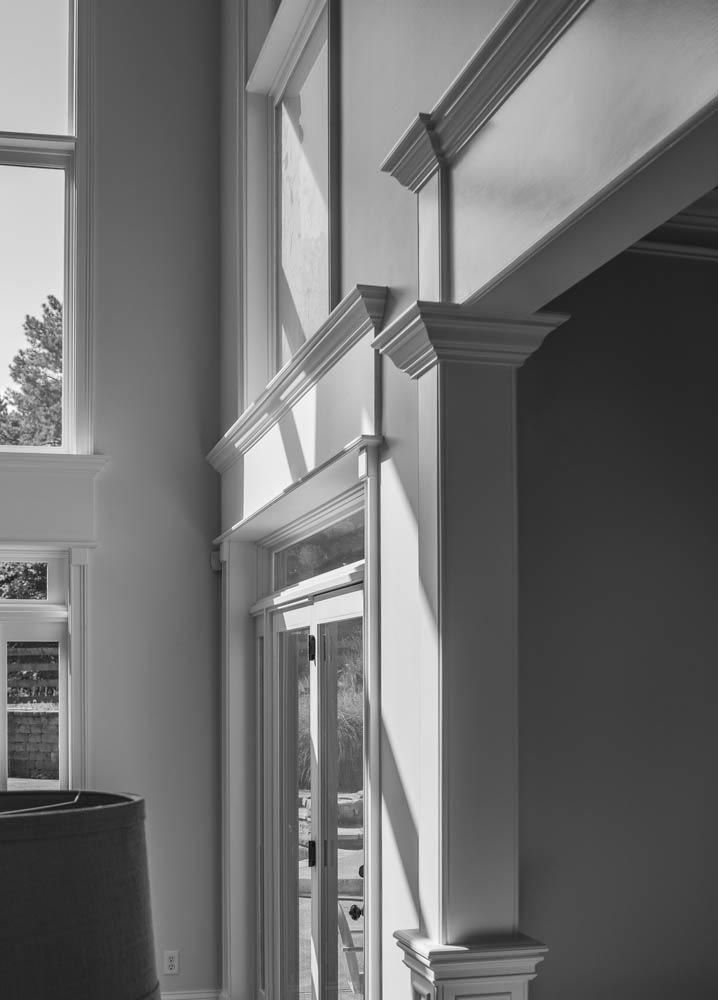 Black and white photo of an interior doorway and window trim with strong sunlight casting shadows on the walls.