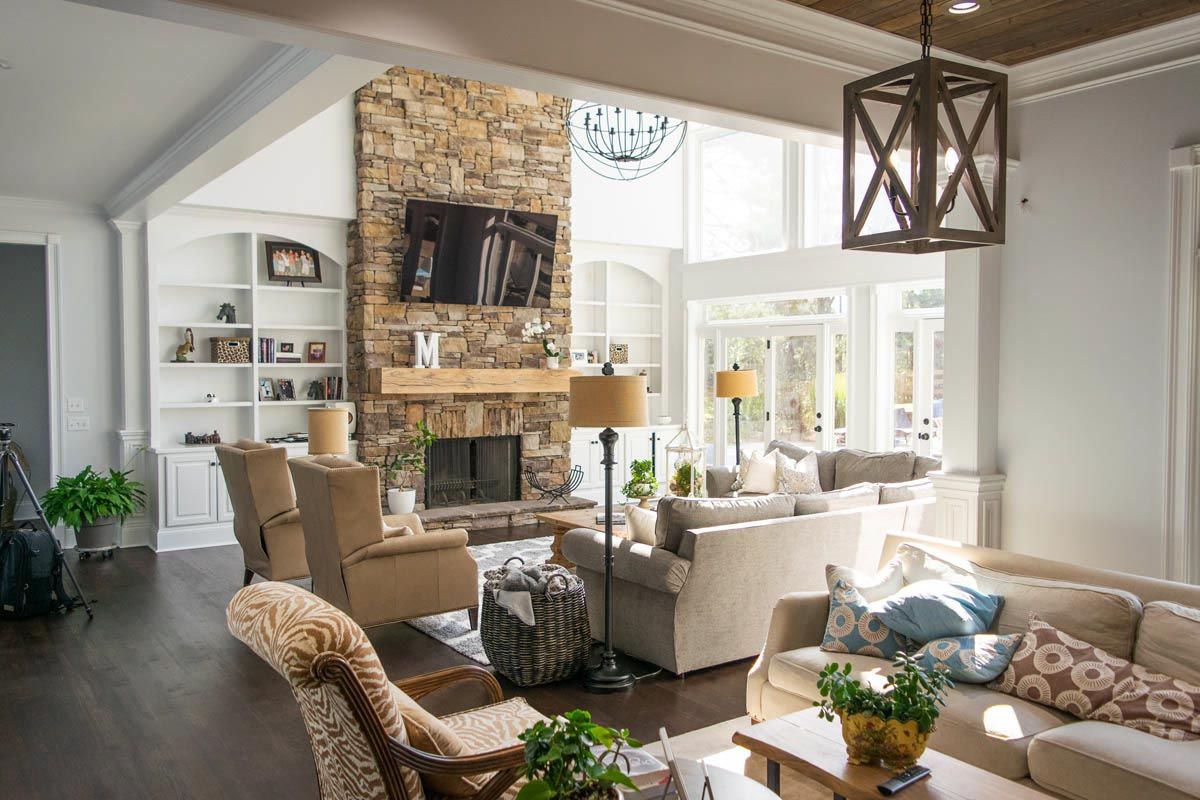 Living room with stone fireplace, built-in shelves, multiple sofas, and large windows.