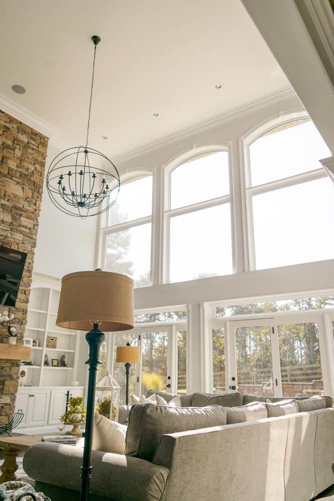 Living room with large windows, stone fireplace, chandelier, and a beige sofa.
