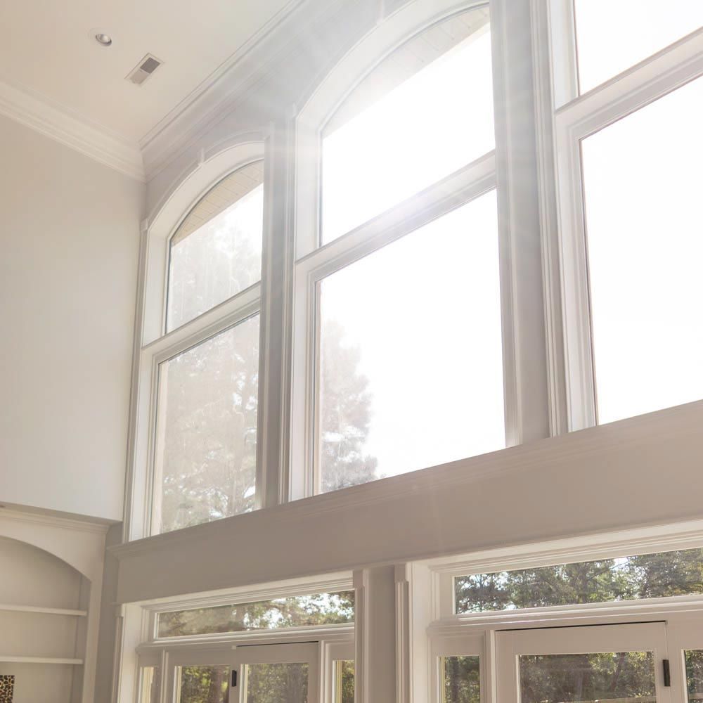 Tall, arched windows with bright sunlight streaming in. White trim, light gray walls.