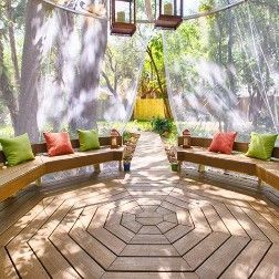 Wooden outdoor seating area with benches, cushions, and sheer curtains.