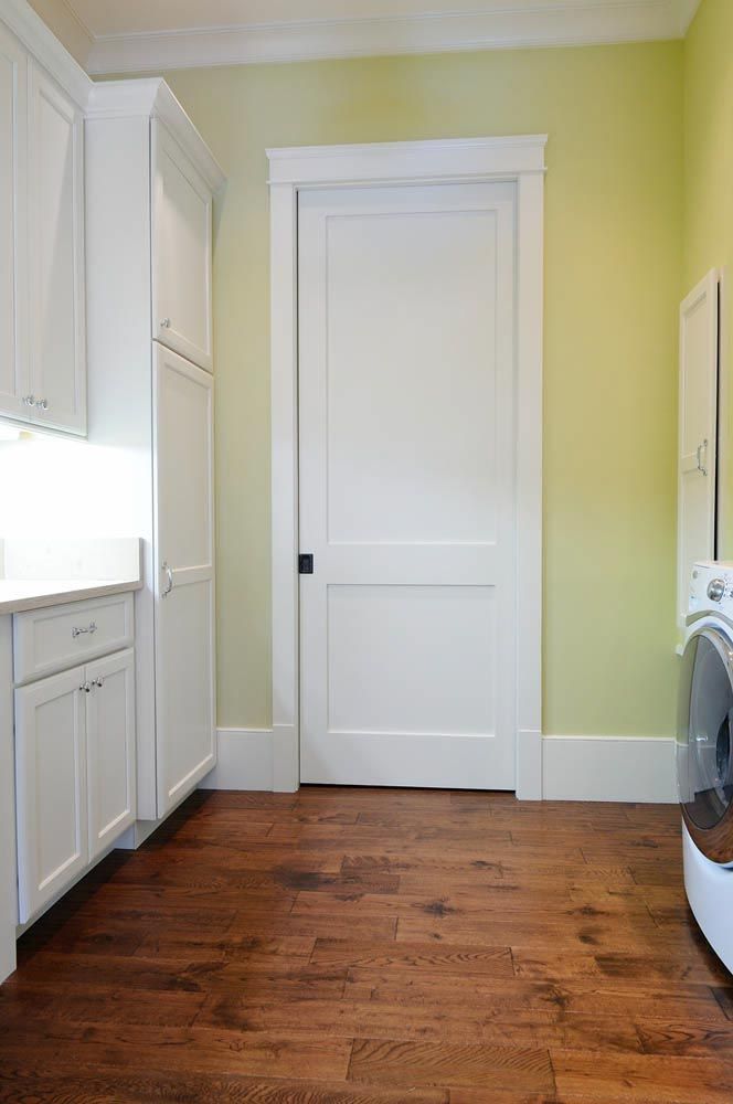 Laundry room with white cabinets, door, and a washing machine, featuring hardwood floors and pale green walls.