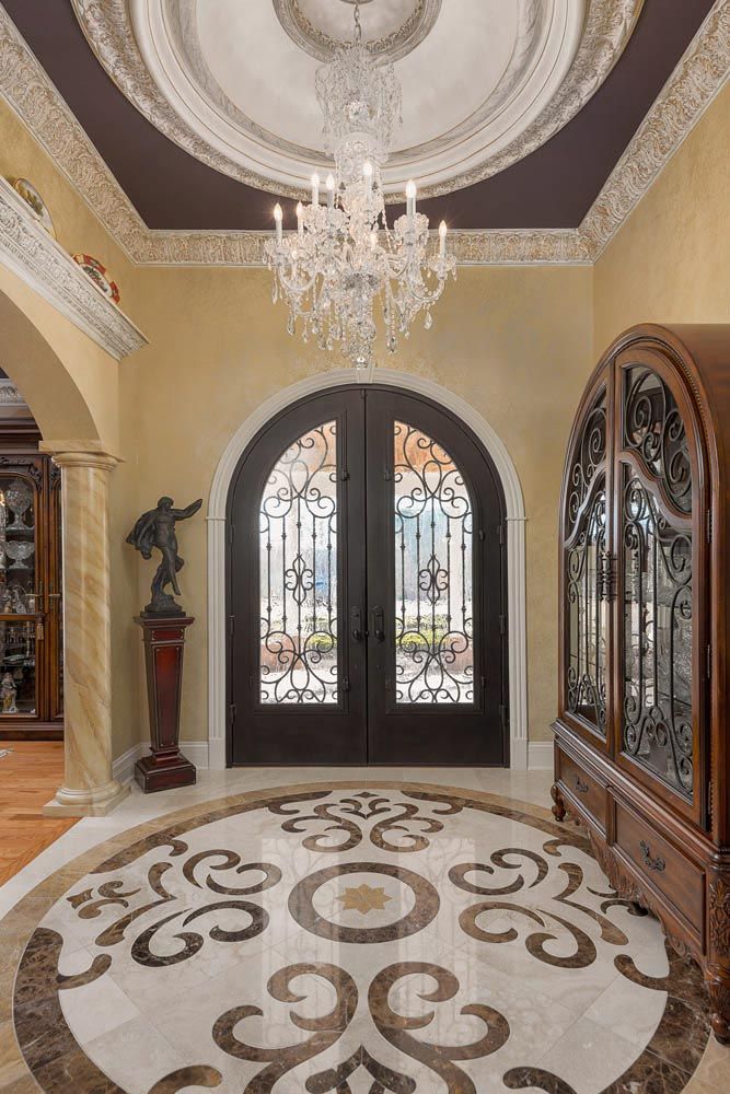 Elegant foyer with arched, wrought-iron doors, chandelier, marble flooring, and wood cabinet.