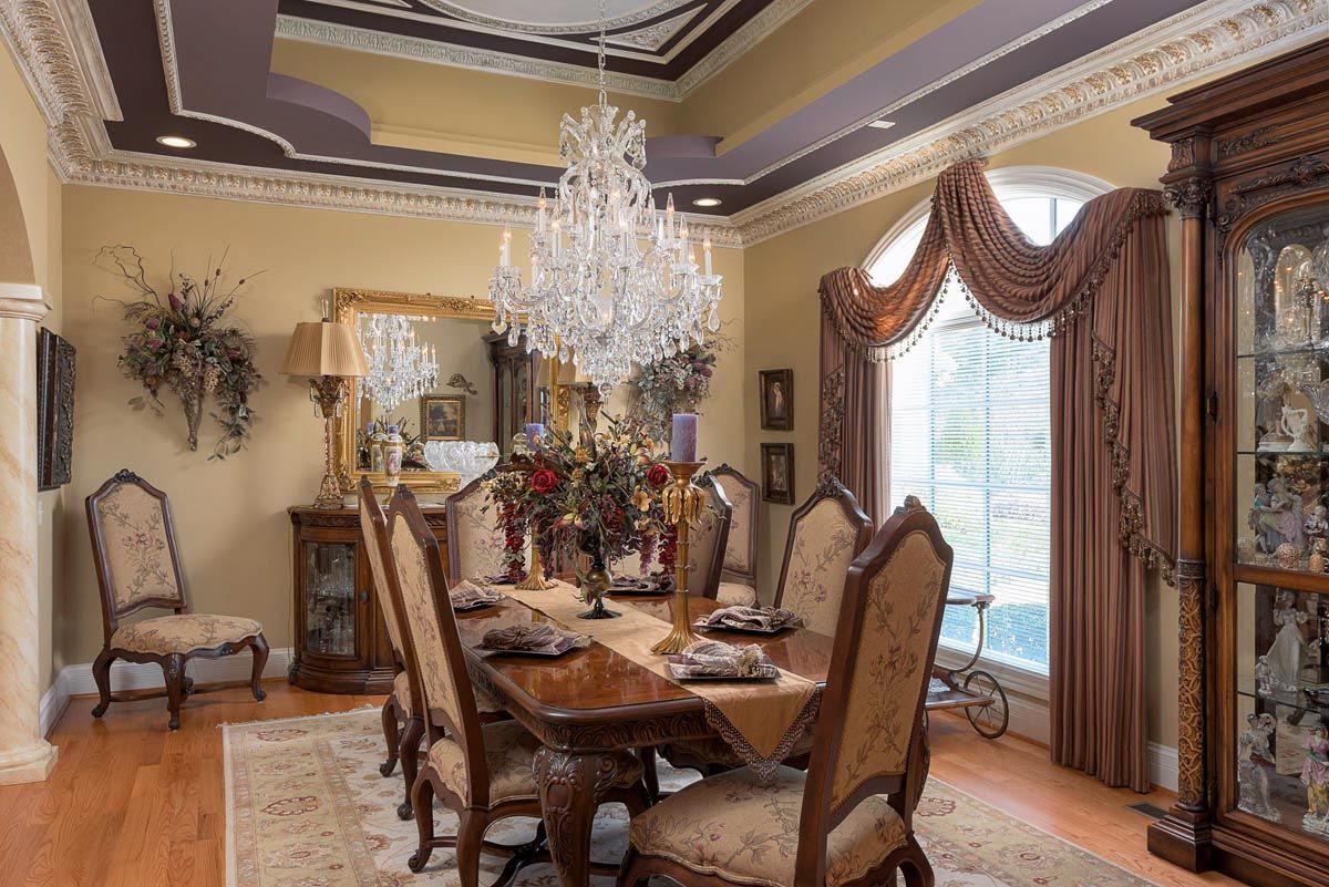Elegant dining room with chandelier, ornate table, chairs, and window with draped curtains.