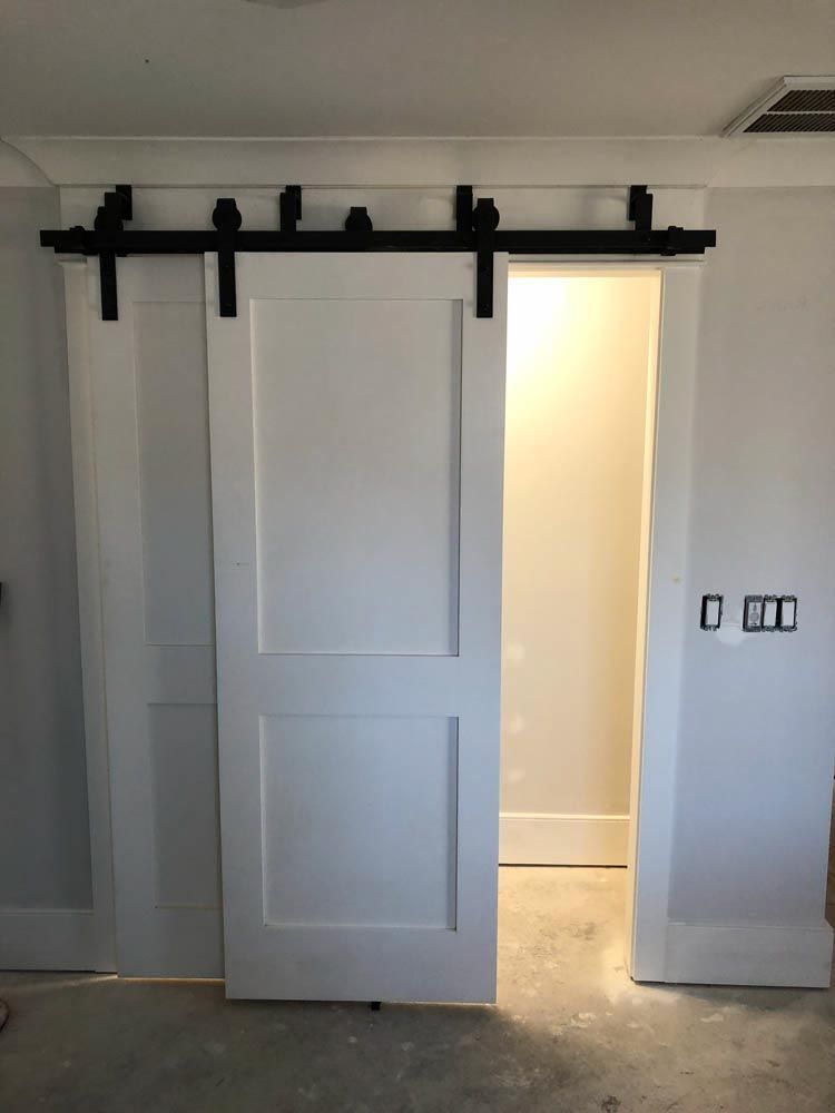 White sliding barn door, black hardware, open to lit room, mounted on white wall.