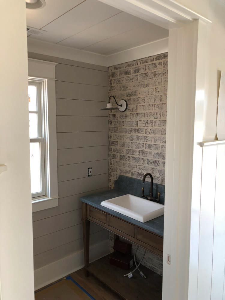 Small bathroom with white brick wall, gray wood paneling, sink, and window.