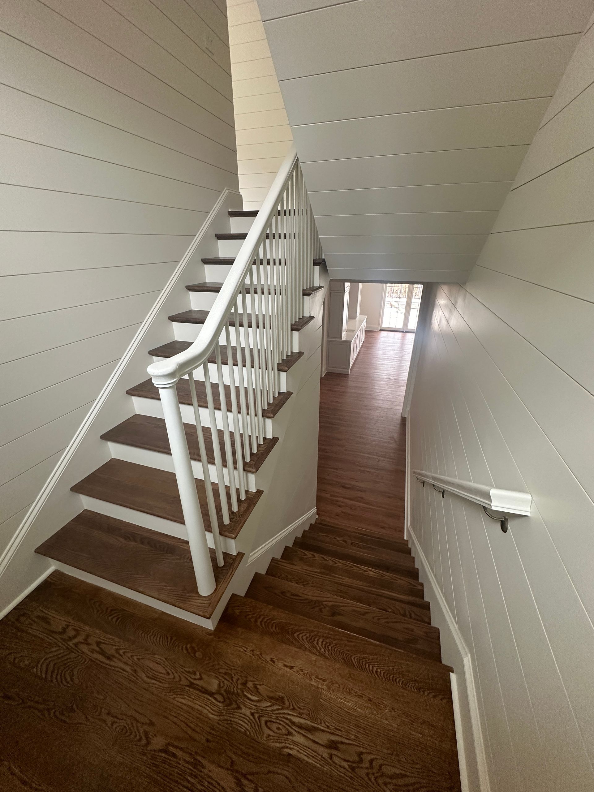 Staircase with wooden steps and white railing, leading to a hallway. White paneled walls.