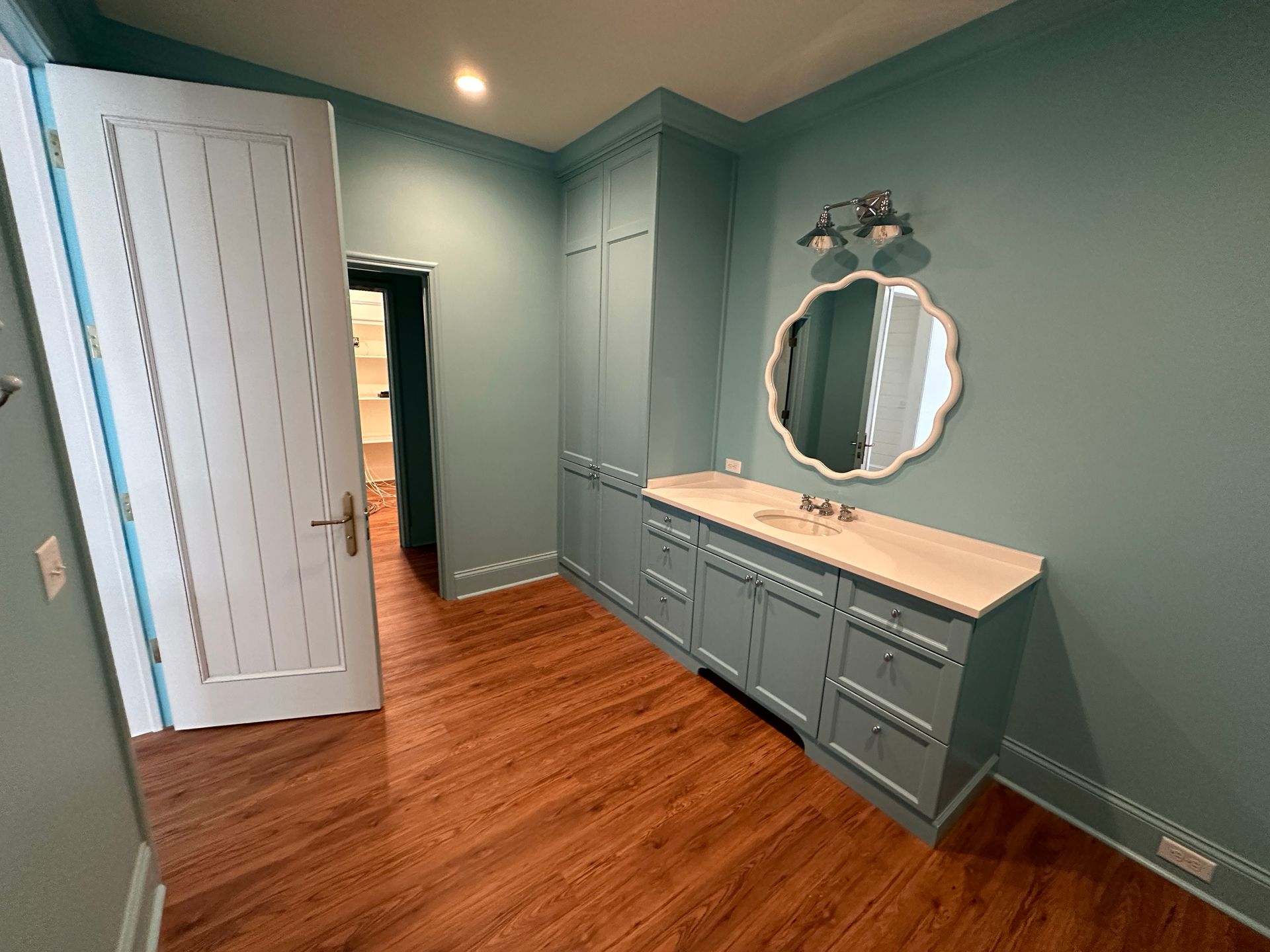Bathroom with blue walls, cabinets, and door, a light-colored countertop, and a decorative mirror over the vanity.