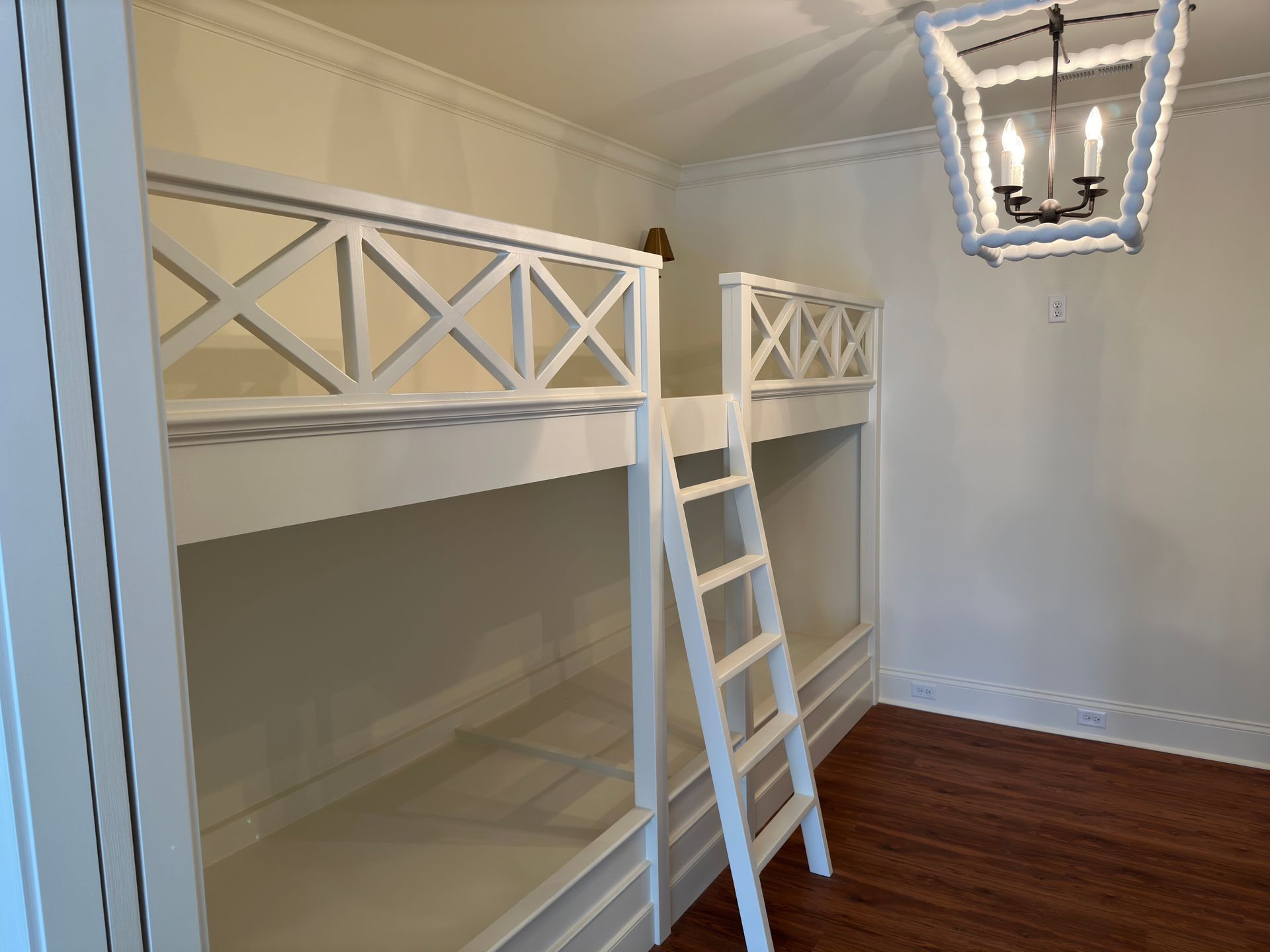 White bunk beds in a room with a hardwood floor and chandelier.