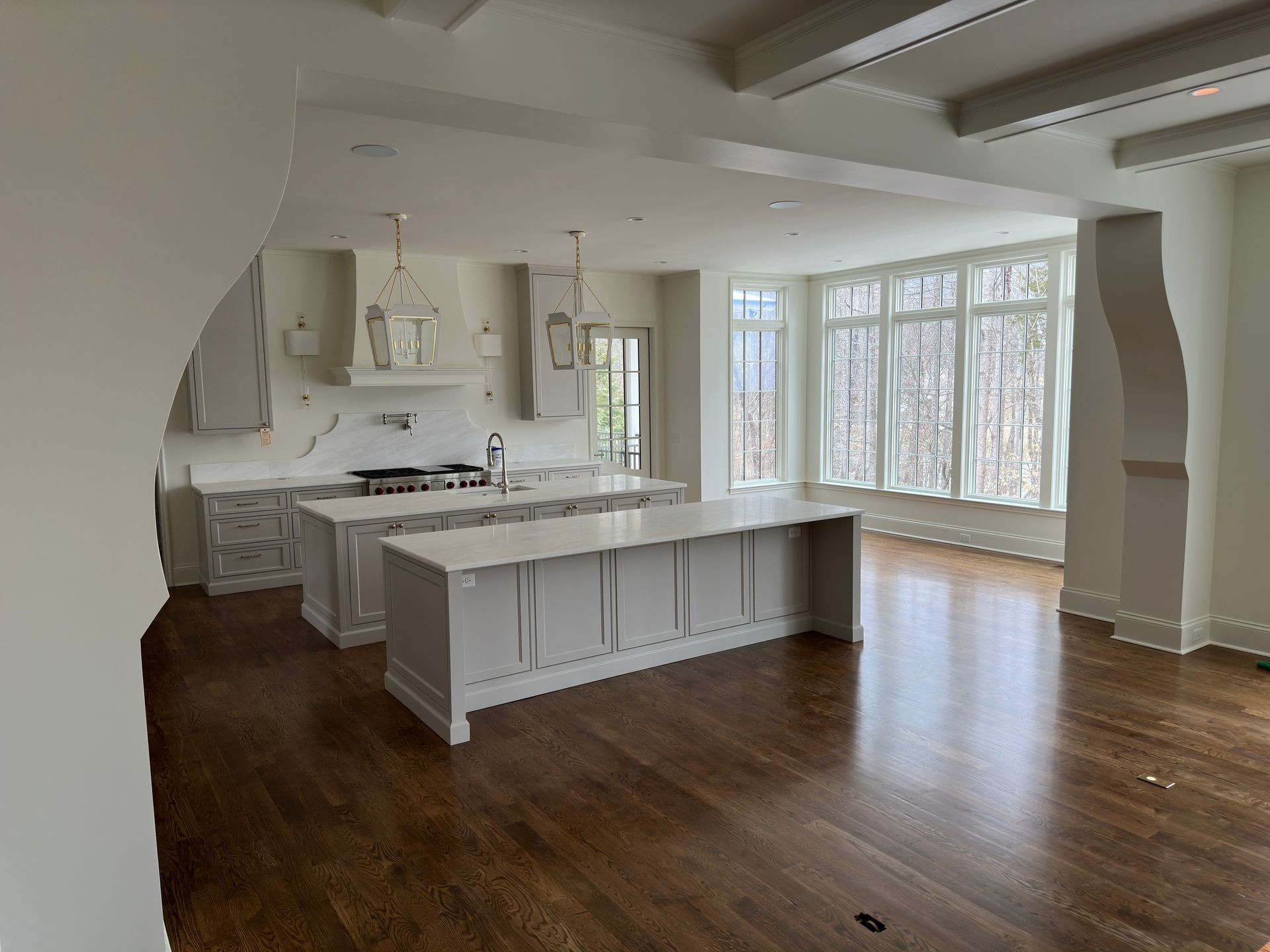 Kitchen with two islands, marble countertops, and large windows overlooking trees. Dark wood floors.