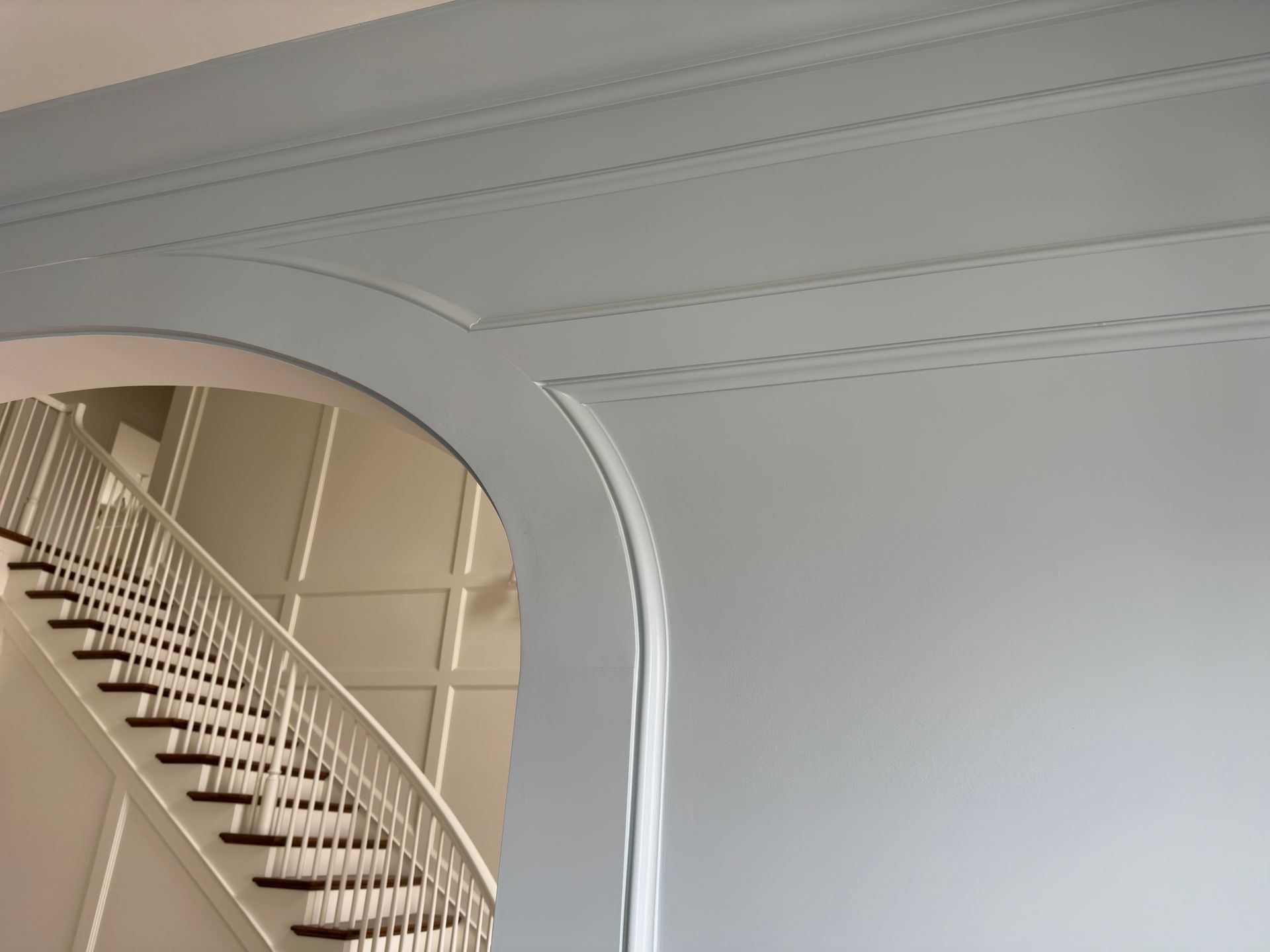 Light blue wall with arched opening revealing a white staircase; ceiling with recessed panels.